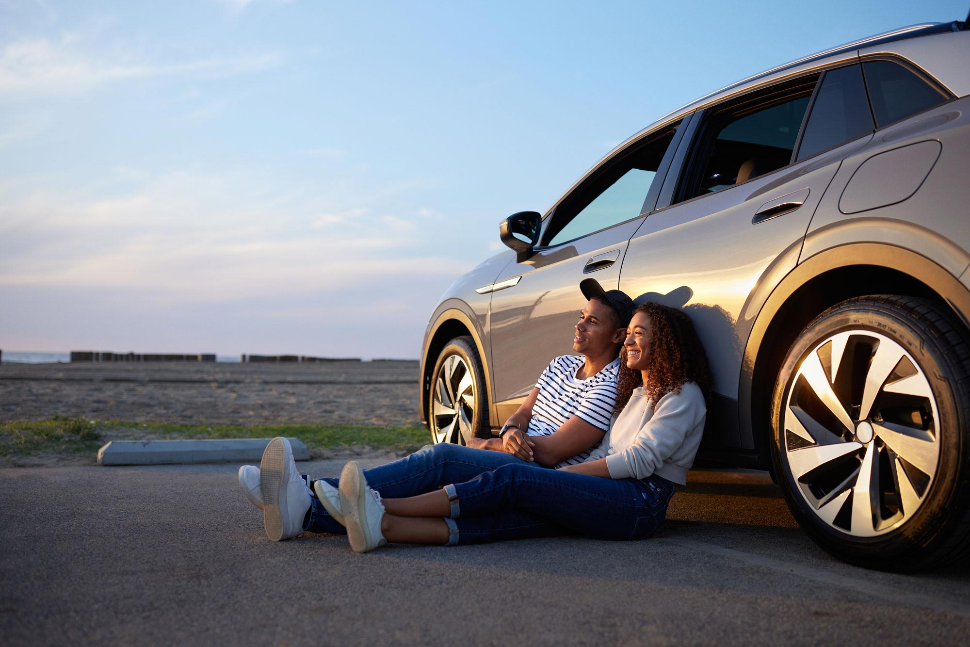 A man and woman sitting on the ground in front of a car